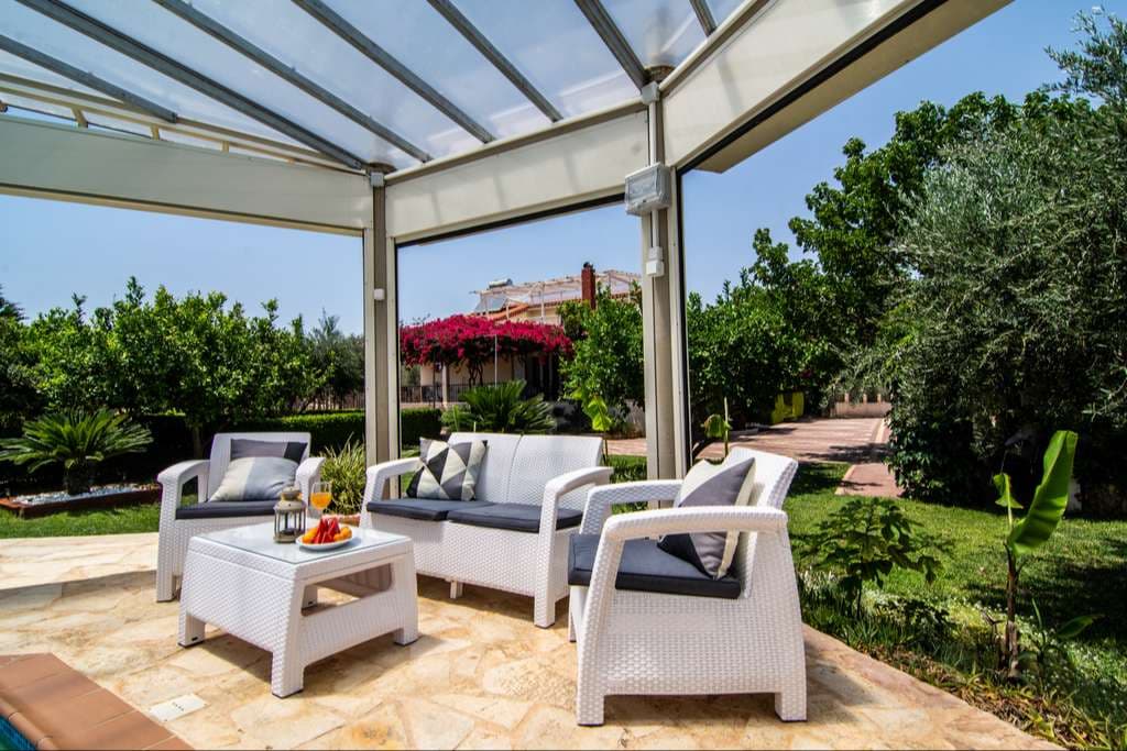 White wicker seating on the shaded terrace beside the lawn and citrus trees